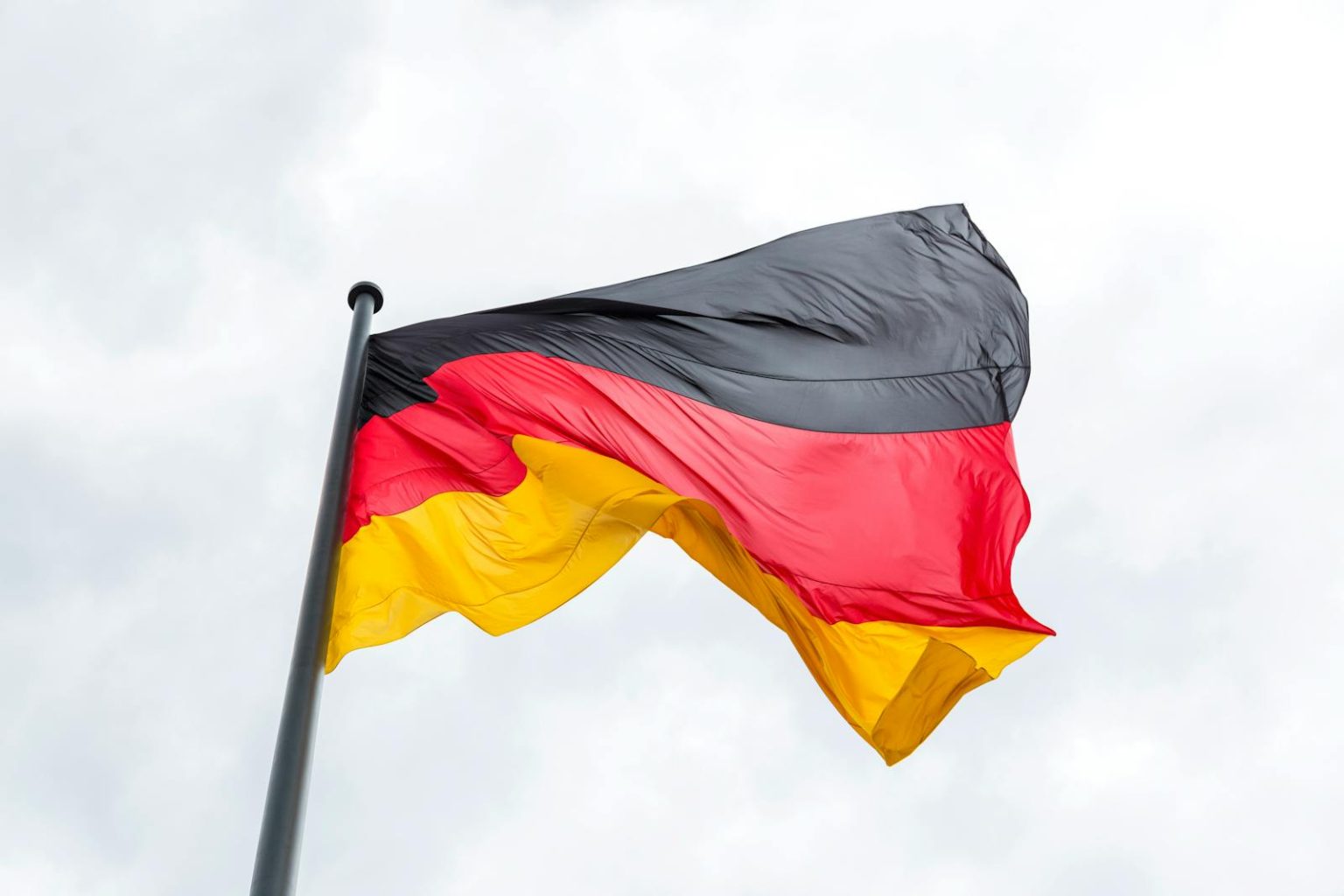 Germany to Reinstate EV Purchase Subsidies With €3 Billion Program From 2026 Vibrant German flag flying against a backdrop of a cloudy sky, symbolizing national pride.