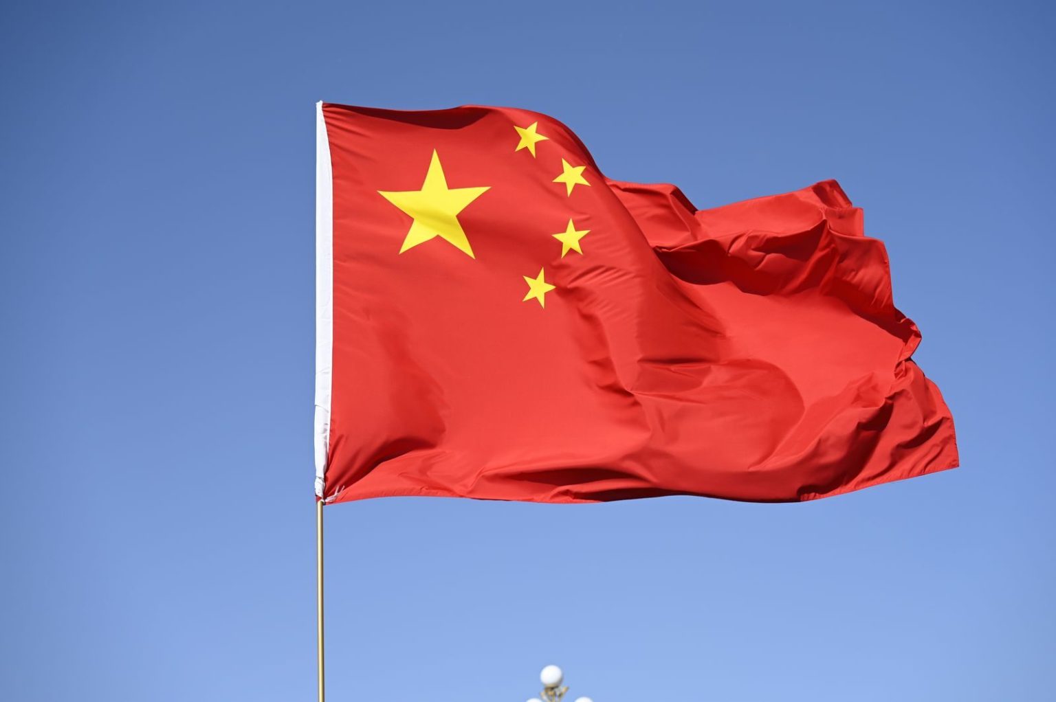 CPCA’s Cui Says China’s Battery Tax Will Encourage Automakers to Expand In-House Cell Production Chinese national flag flying high against a clear blue sky, symbolizing unity and pride.